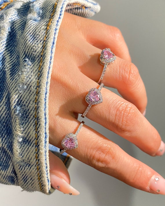 Hand wearing a pink heart-shaped ring with a denim jacket background